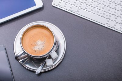 Kaffeetasse umrahmt von Tastatur, Smartphone und Tablet